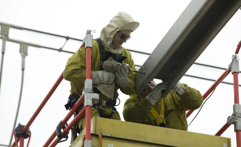 Photo de deux techniciens perçant un trou à la perceuse dans une structure métallique