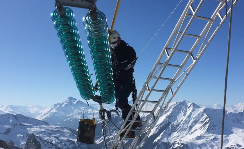 Photo d'un lignard en train d'intervenir sur un isolateur avec des montagnes enneigées en arrière-plan
