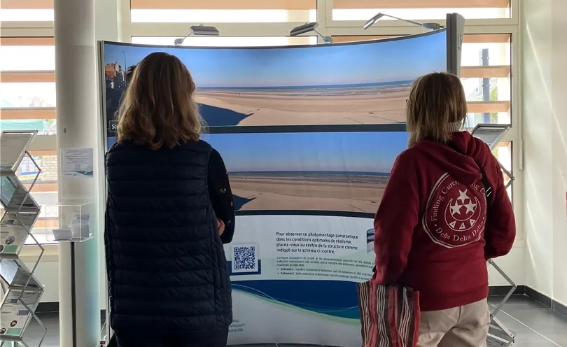 Photo de deux personnes en train de lire le panneau d'informations du projet éolien en mer de Dunkerque