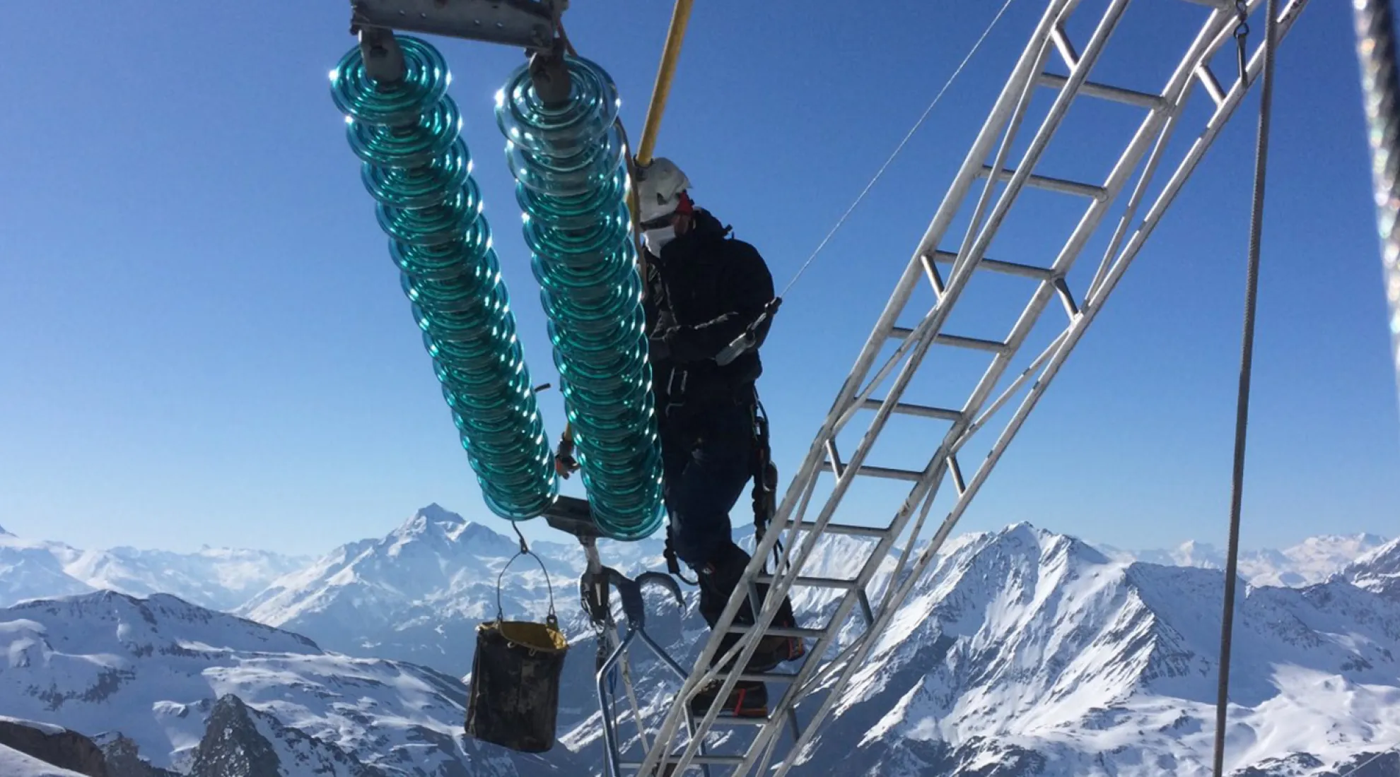 Photo d'un lignard en train d'intervenir sur un isolateur avec des montagnes enneigées en arrière-plan