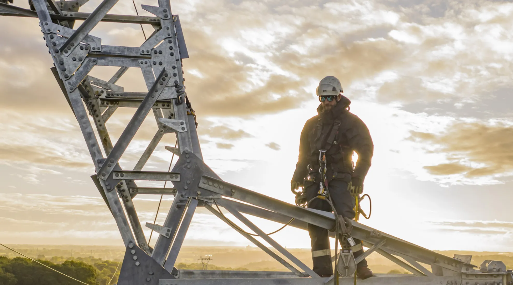 Technicien effectuant une maintenance en hauteur sur une installation électrique, avec une météo ensoleillée.