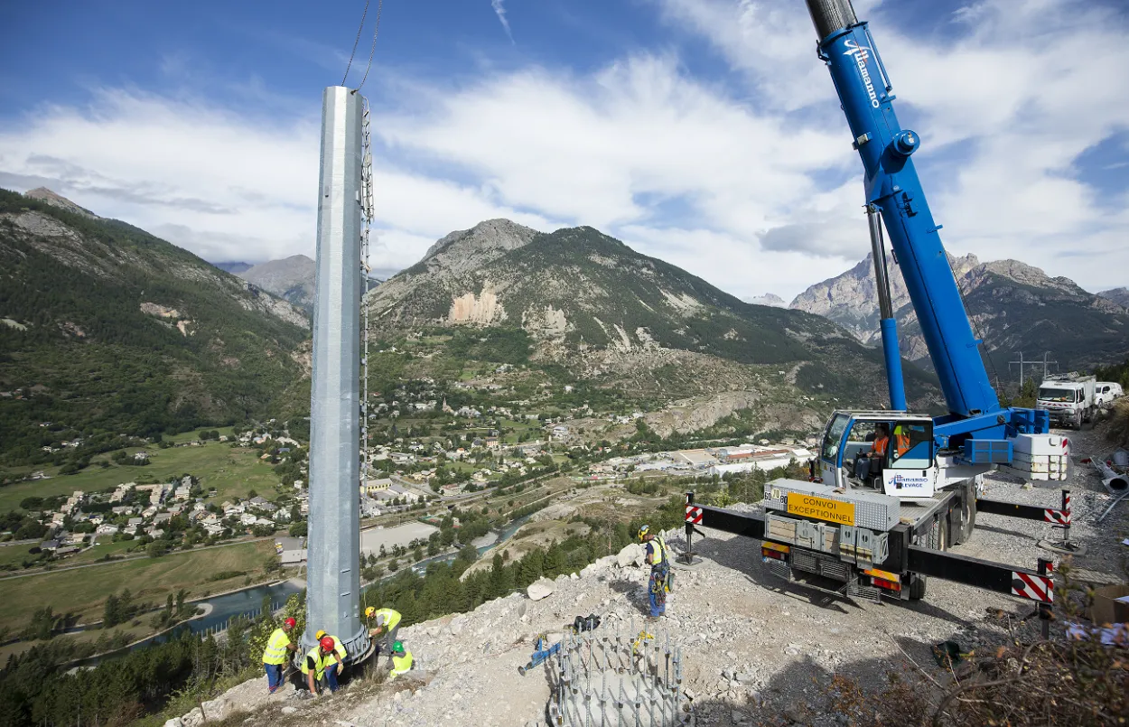 Photo d'un pied de pylône, soulevé par une grue, sur le point d'être fixée par des techniciens