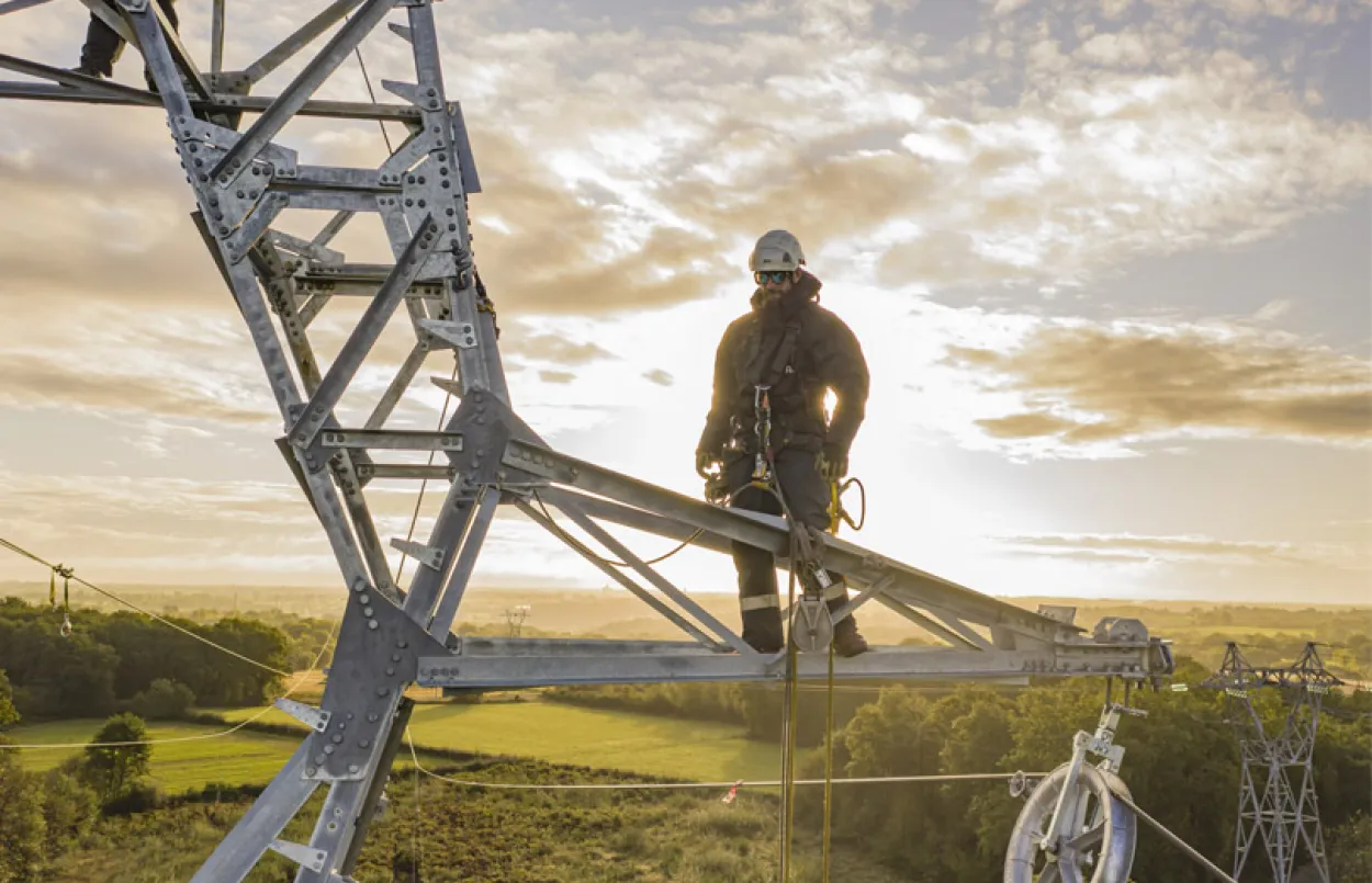 Un technicien effectuant une maintenance sur une installation électrique en hauteur, avec une météo ensoleillée.