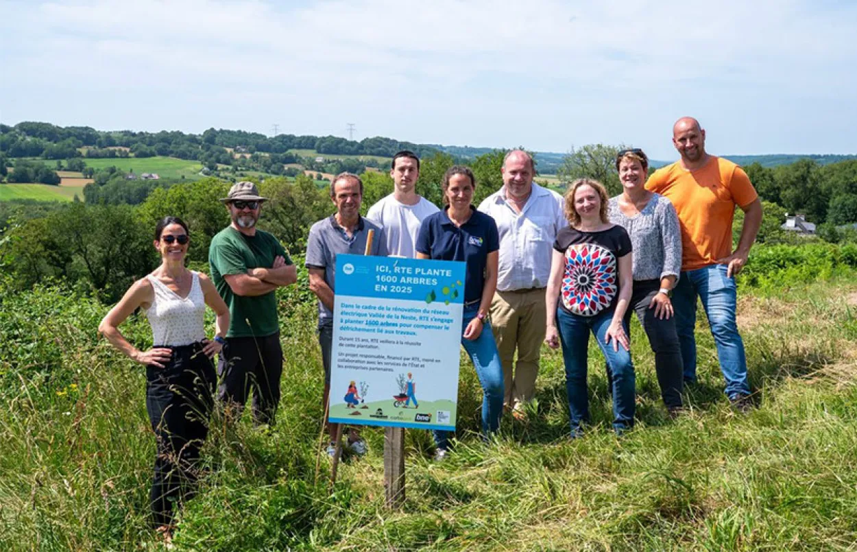 Groupe de neuf personnes debout dans un champ verdoyant, posant derrière un panneau annonçant la plantation d’arbres par RTE en 2025. Le paysage en arrière-plan montre des collines du Béarn.