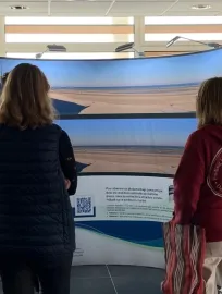 Photo de deux personnes en train de lire le panneau d'informations du projet éolien en mer de Dunkerque