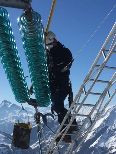 Photo d'un lignard en train d'intervenir sur un isolateur avec des montagnes enneigées en arrière-plan